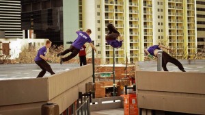 Casey Wilson flipping off one rooftop to another. This move is called a side flip.