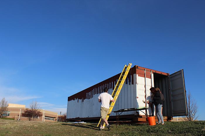Architecture students taking the first steps in the project, painting the first layer or primer onto the container. 